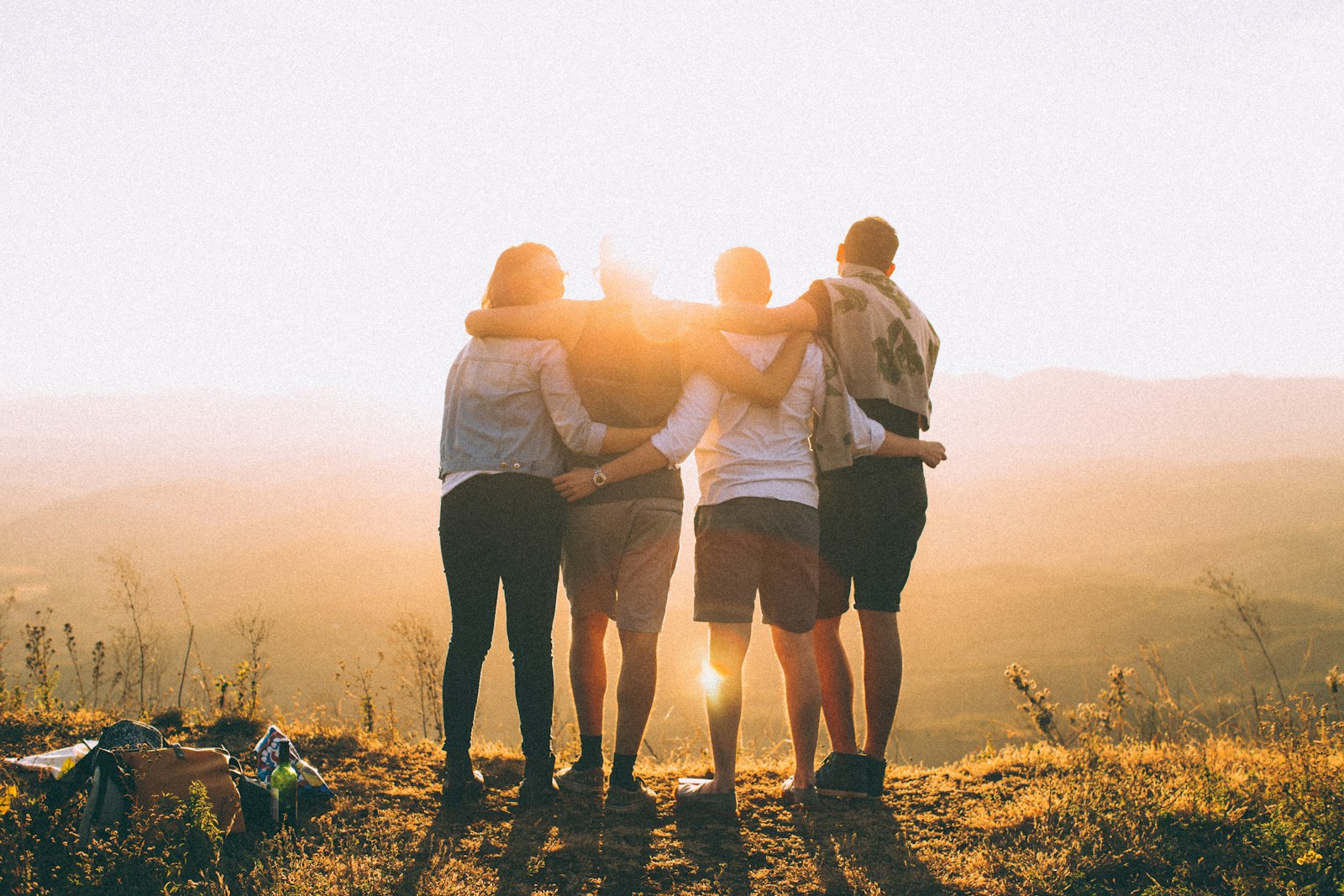 Four people standing arm-in-arm on a hillside watching the sunset over rolling hills.